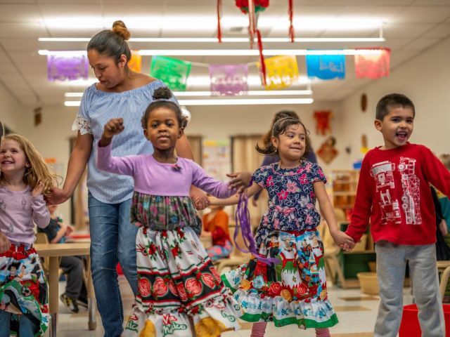 Children hold hands as they play in a decorated room with a teacher