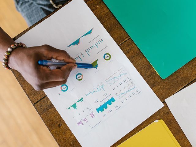 Aerial view of a desktop with a person pointing to a chart on a piece of paper