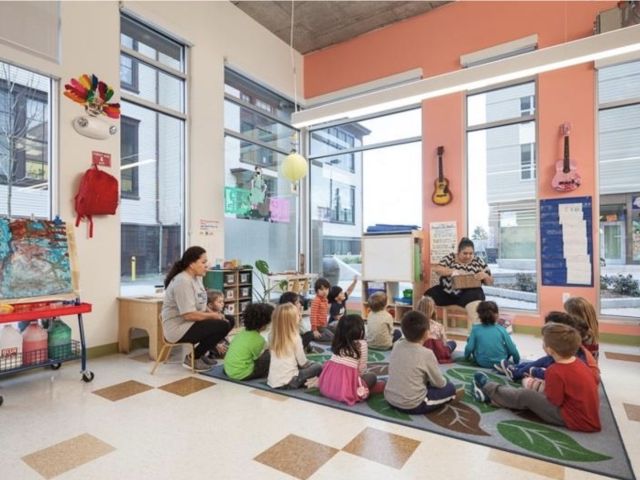 Children sit on the floor as they listen to an instructor in a colorful classroom