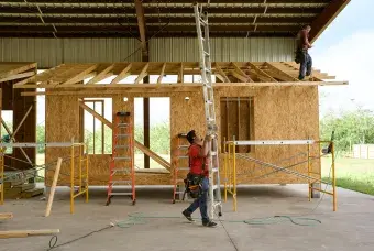 Construction worker carries a ladder in front of a home being built