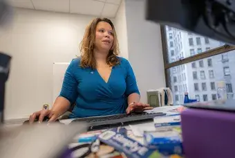 A woman in a teal blouse sitting at a desk working on the computer